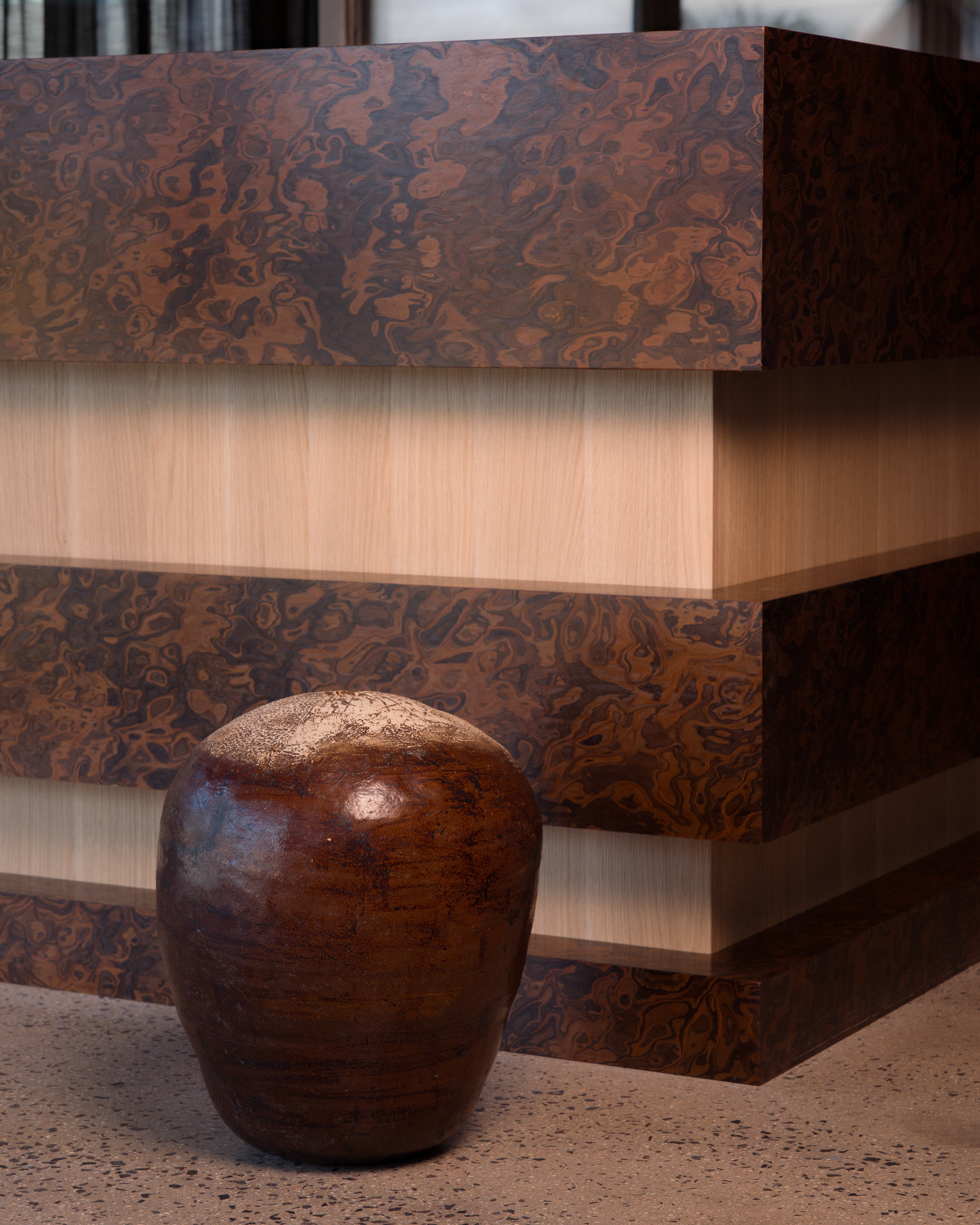 Burl wood veneer reception desk with natural oak inlay detail and handcrafted ceramic vessel — luxury commercial interior design detail by Studio Nicholas Noosa Queensland Australia