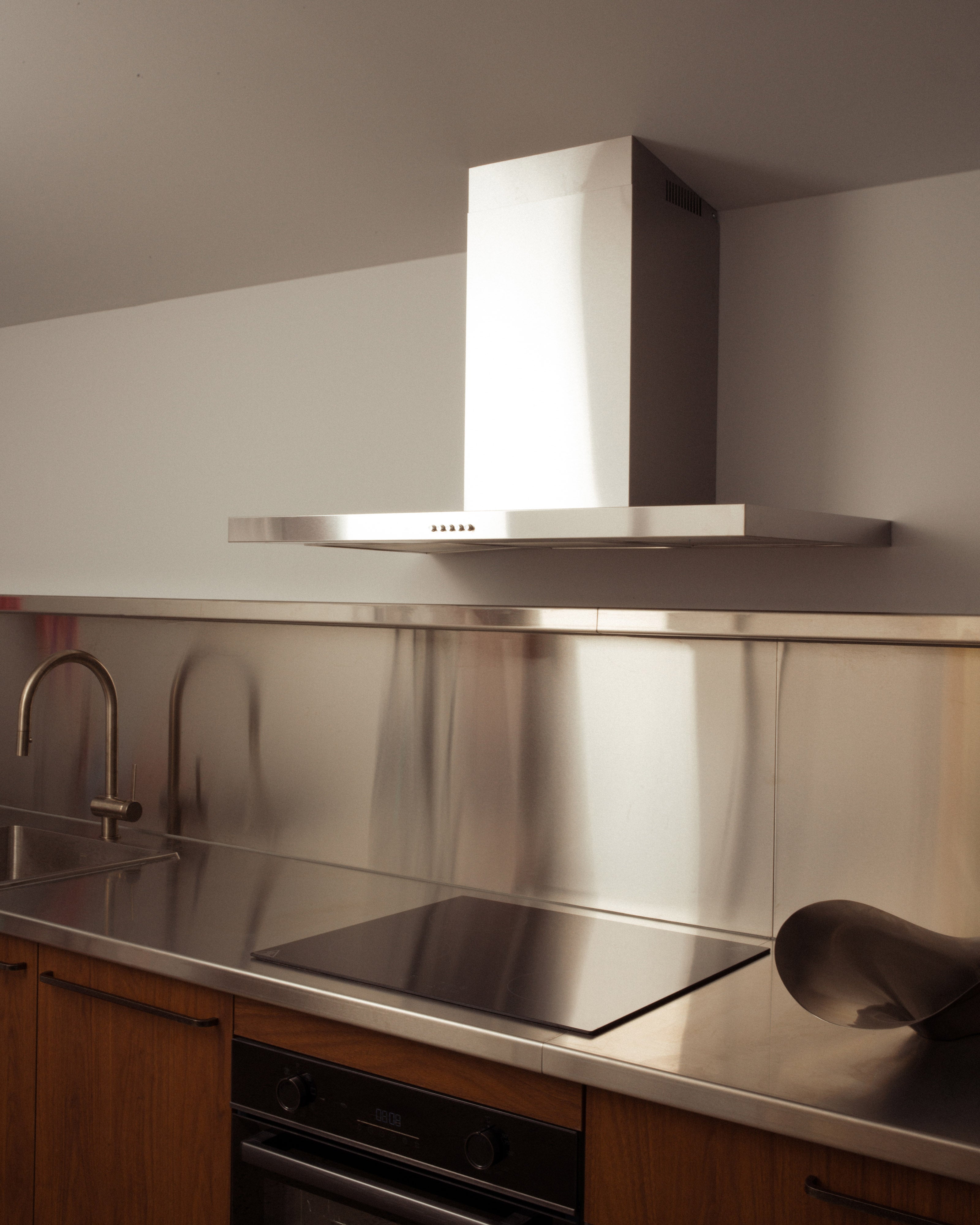 Contemporary kitchen with stainless steel rangehood and splashback, induction cooktop, integrated oven, gooseneck tap, and warm timber cabinetry — residential kitchen interior design by Studio Nicholas Noosa Queensland Australia