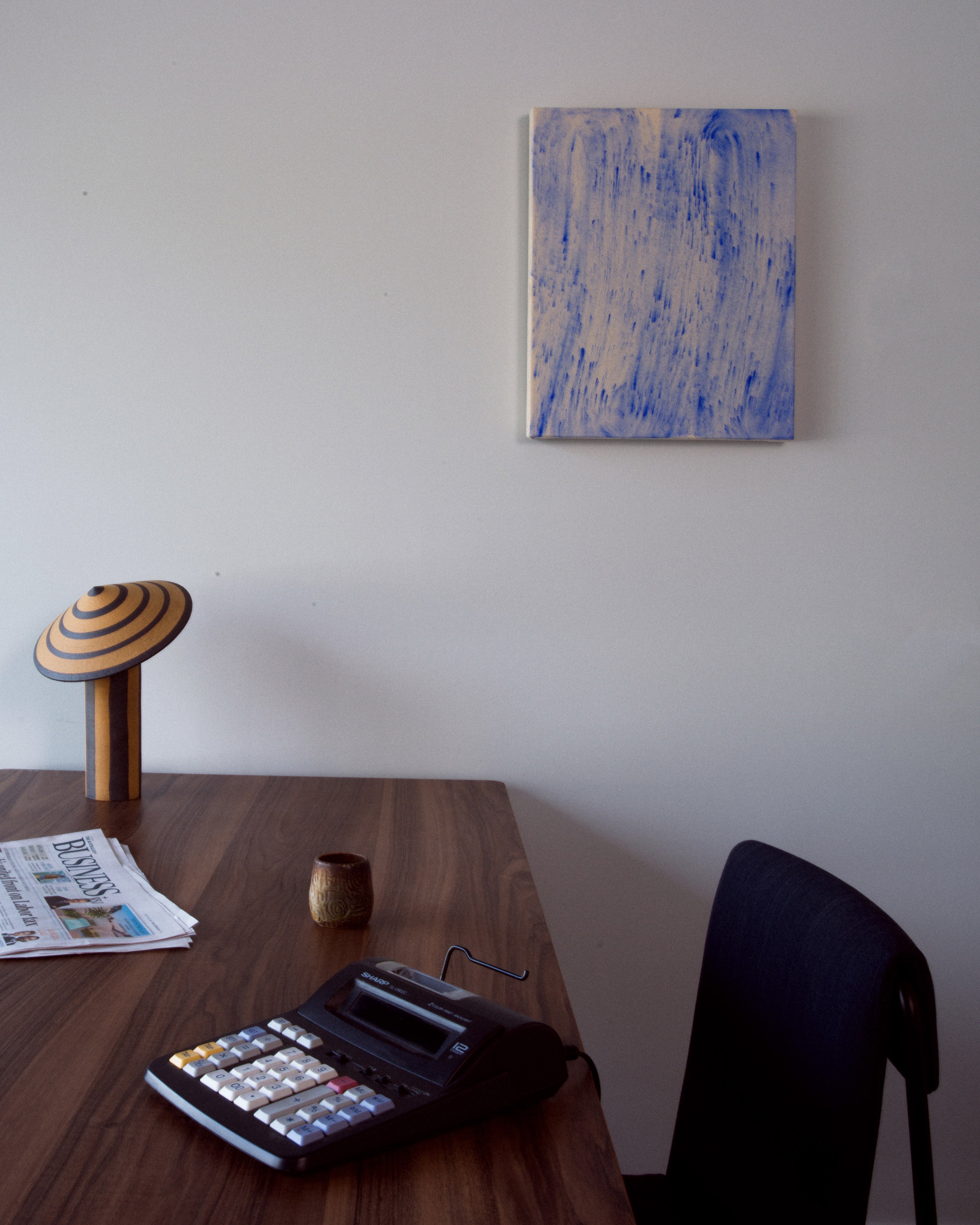 Dark timber office desk styled with striped mushroom table lamp, small ceramic vessel, and calculator beneath a blue and cream abstract artwork on white wall — residential and commercial interior design styling by Studio Nicholas Noosa Queensland Australia